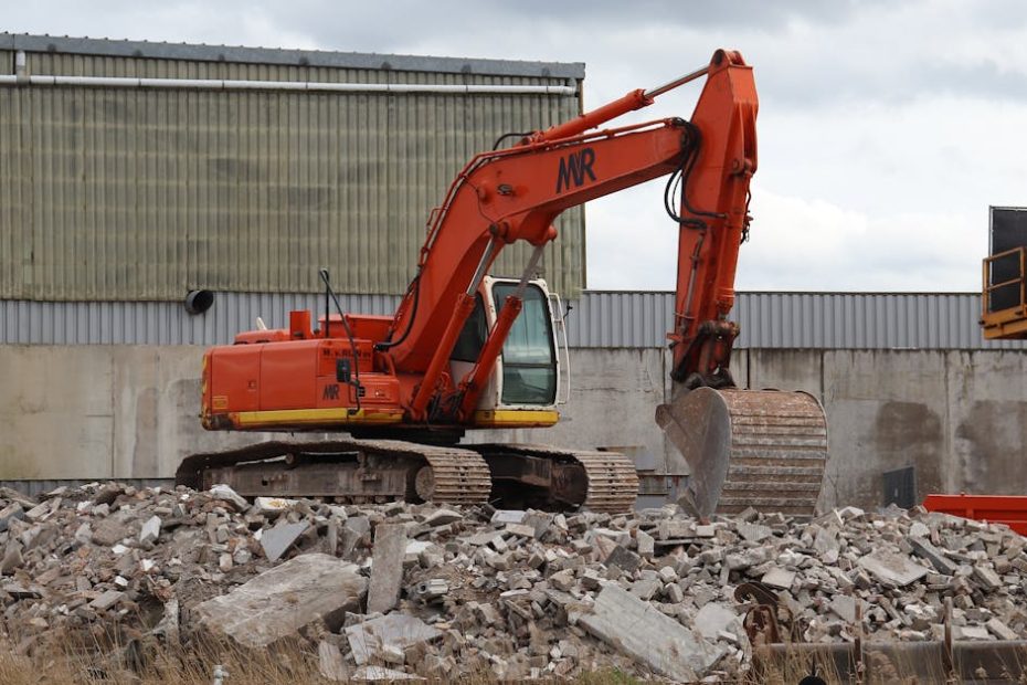 Orange excavator on a demolition site amidst rubble, showcasing construction machinery at work.