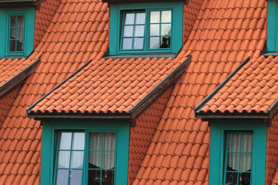 Close-up of an orange tiled roof with green framed dormer windows, creating a colorful architectural contrast.