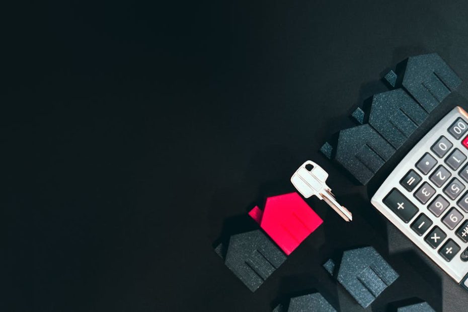 Real estate concept image featuring a calculator, houses, and a key on a black background.