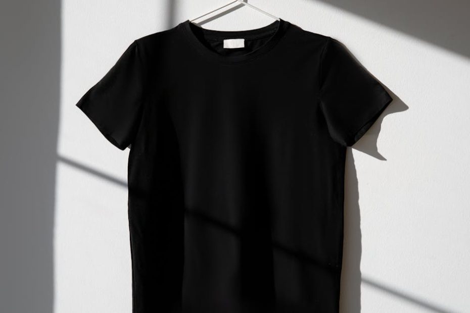 Minimalist image of a black t-shirt on a hanger with dramatic shadows on a white wall.