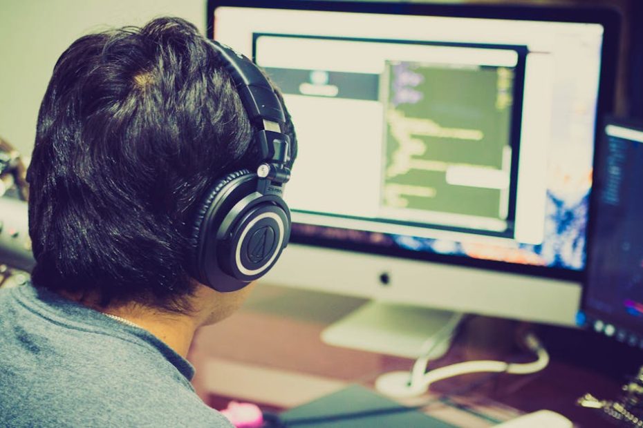 A programmer with headphones focuses on coding at a computer setup with dual monitors.