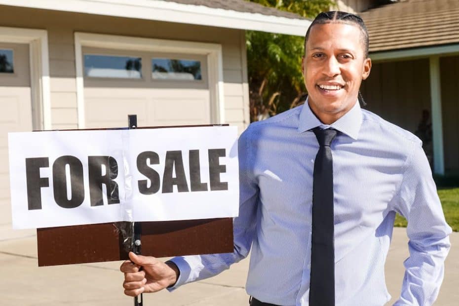 Smiling real estate agent with a for sale sign in front of a house.