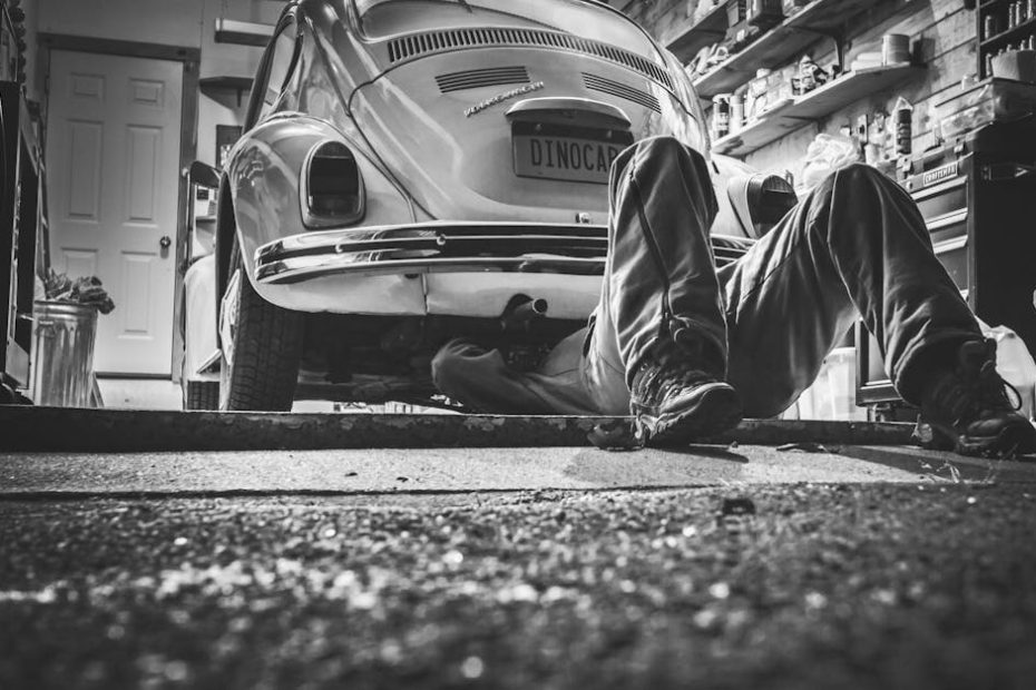 Mechanic working beneath a classic Volkswagen Beetle in a vintage garage setting.