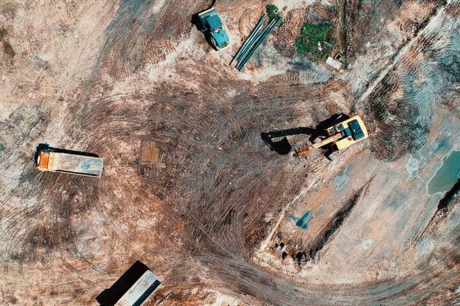 High-angle aerial view of construction site with earthmoving equipment and trucks.