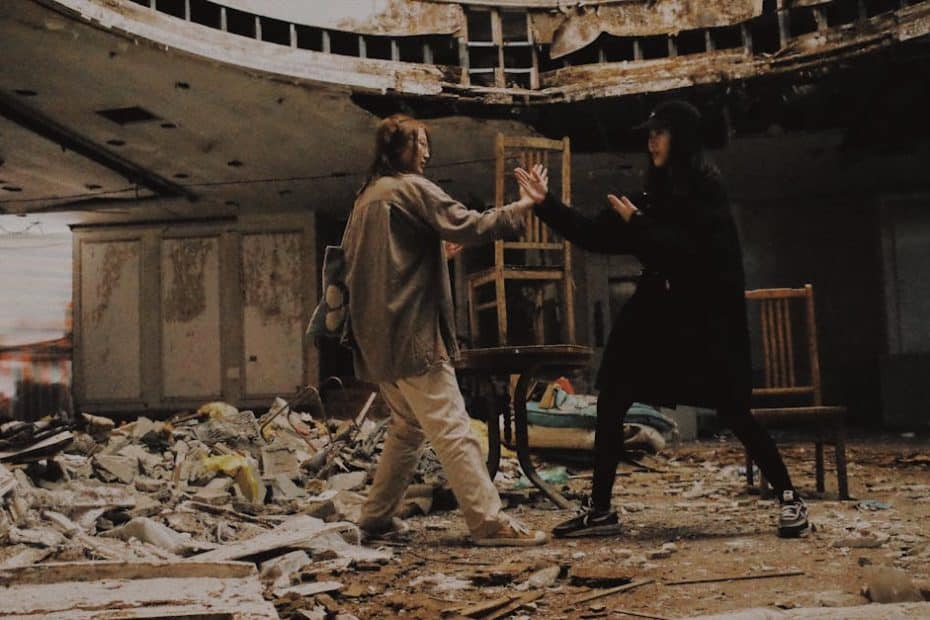 Two individuals pretend to fight in an abandoned, decaying building filled with rubble.