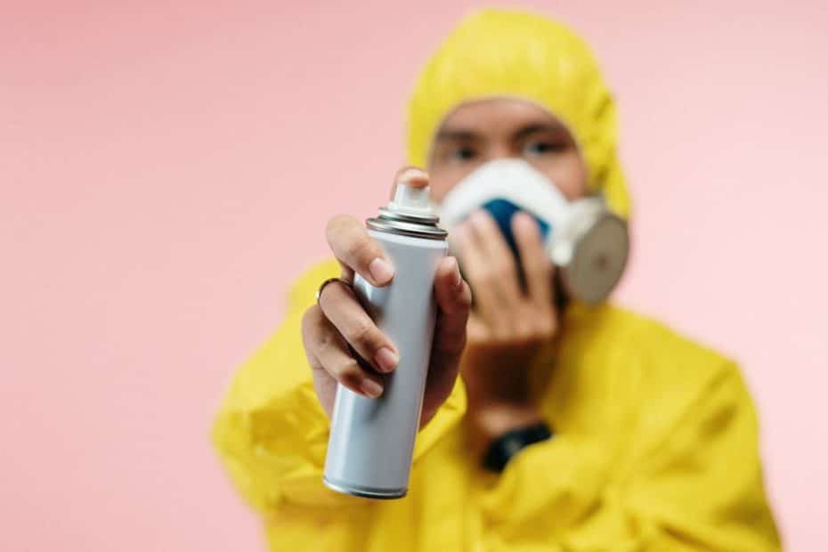 Individual in yellow hazmat suit sprays disinfectant, focusing on hygiene and safety.