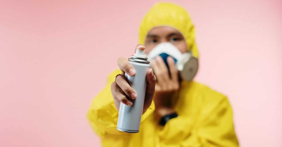 Individual in yellow hazmat suit sprays disinfectant, focusing on hygiene and safety.