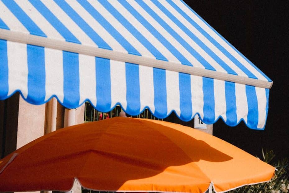 Vibrant blue striped awning and orange umbrella providing summer shade outdoors.
