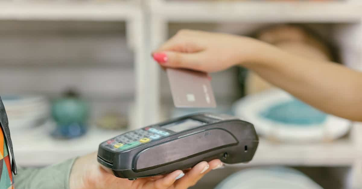A hand using a credit card for payment at a point of sale terminal, close-up view.