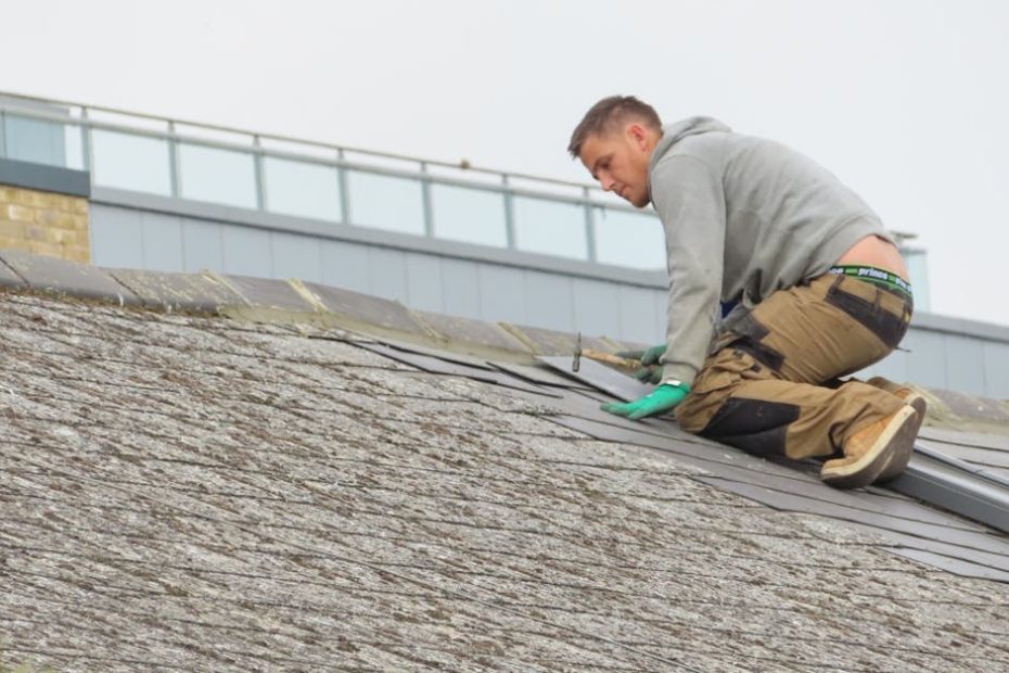 Construction worker installing shingles on a rooftop. Outdoor building maintenance.