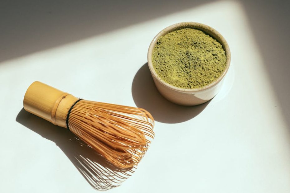 Minimalist composition featuring matcha powder and bamboo whisk in sunlight.