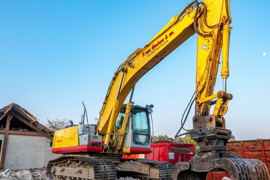 A large yellow excavator working amidst rubble at a construction site under a clear blue sky.
