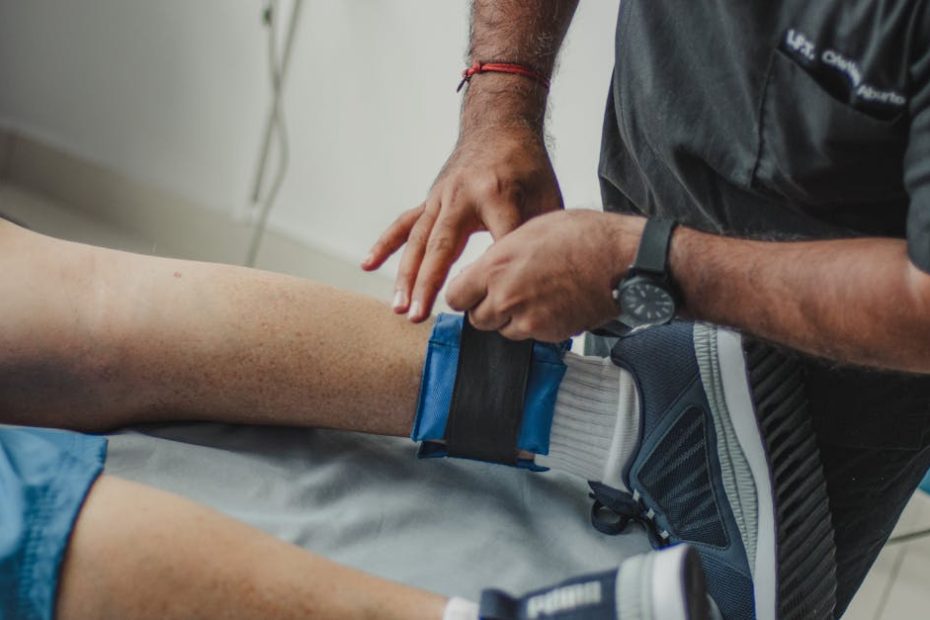 A physiotherapist adjusts a leg strap on a patient in a clinical setting.