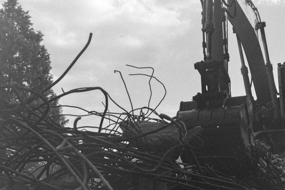 Monochrome image of an excavator engaged in demolition amidst rubble and debris.