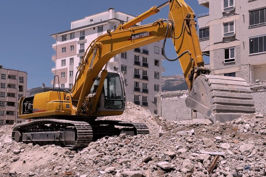 Yellow excavator working on urban construction site amidst rubble and buildings in Kahramanmaraş, Türkiye.