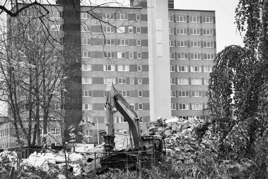A construction excavator amidst rubble in front of a high-rise building.
