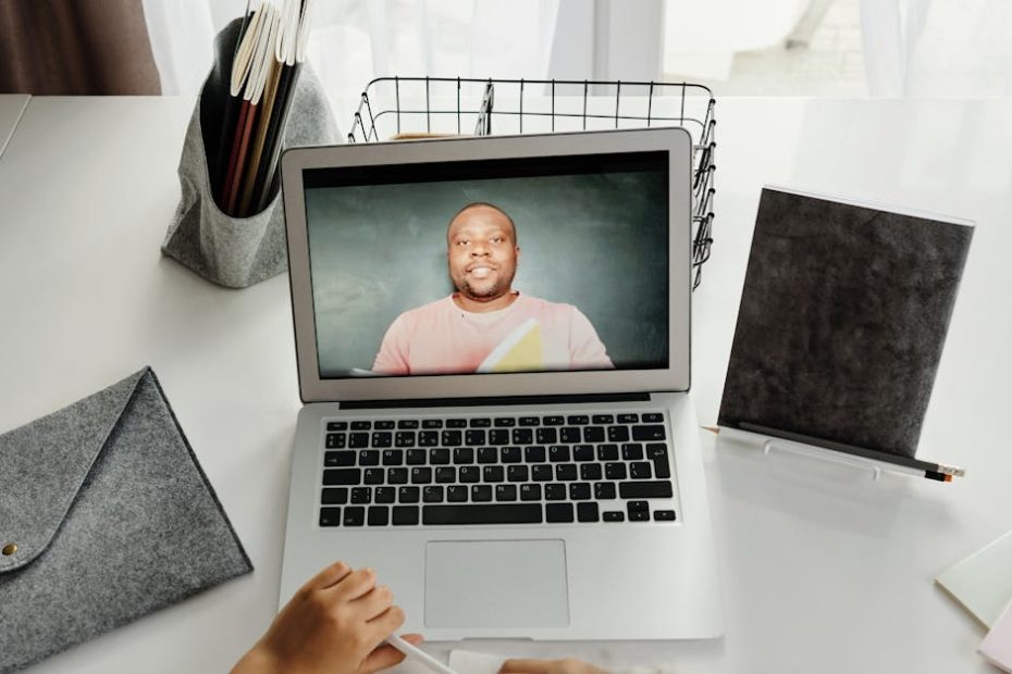 A student participates in a virtual class with a teacher on a laptop screen.