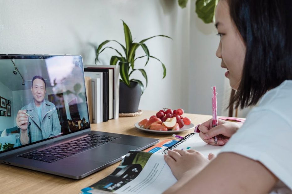 Young girl engaged in online learning via video call, studying with laptop and notes.