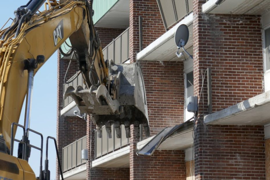 Excavator demolishing a brick residential building in an urban area.