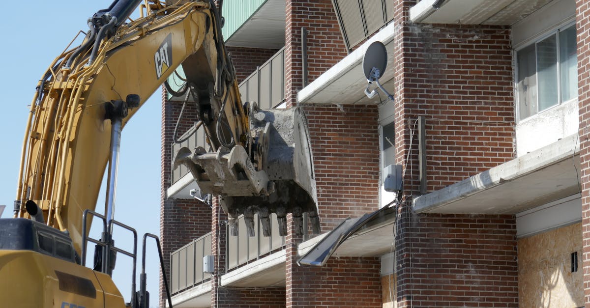 Excavator demolishing a brick residential building in an urban area.
