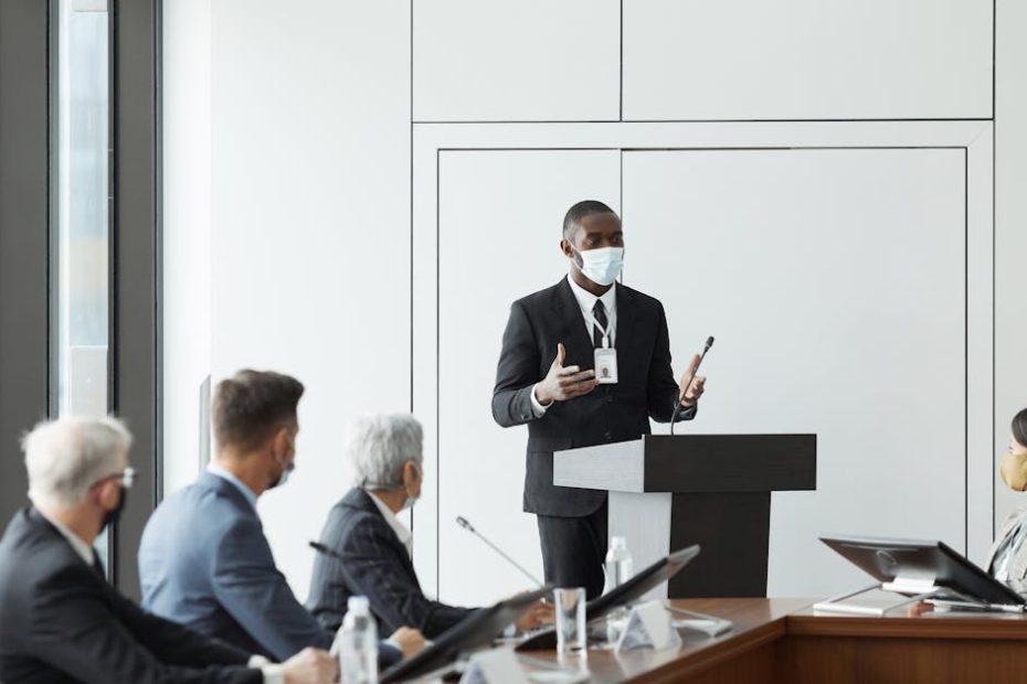 Business professionals in masks hold a meeting indoors, highlighting new normal practices during pandemic times.