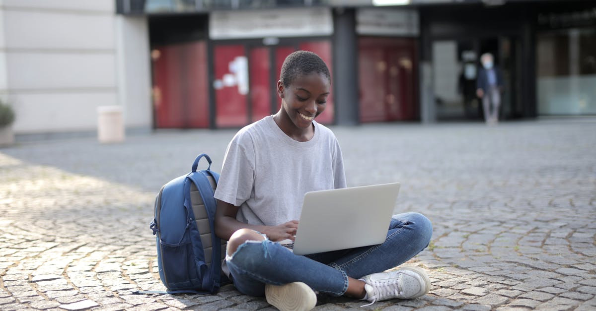Smiling woman sitting on cobblestone street with laptop, engaging in online learning outdoors.