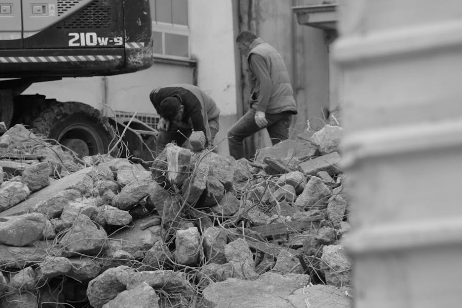 Black and white photo of workers and heavy machinery at a demolished construction site.