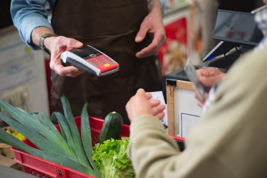 Close-up of customer paying for groceries with produce at a store checkout counter.