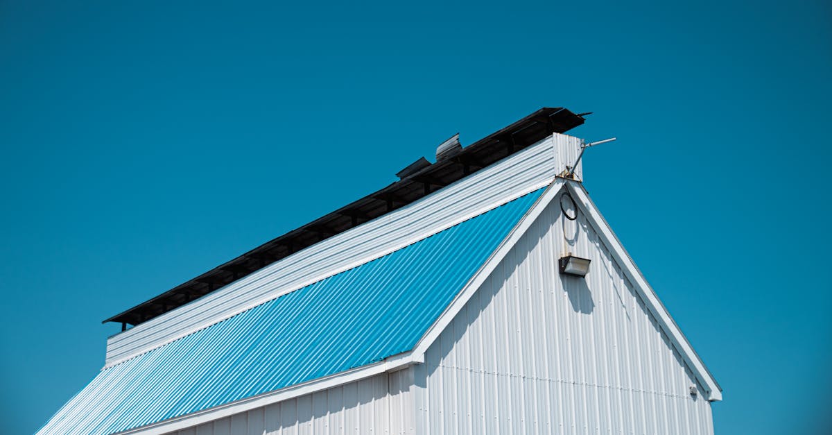 A white barn with a blue metal roof under a bright clear sky in Montreal.