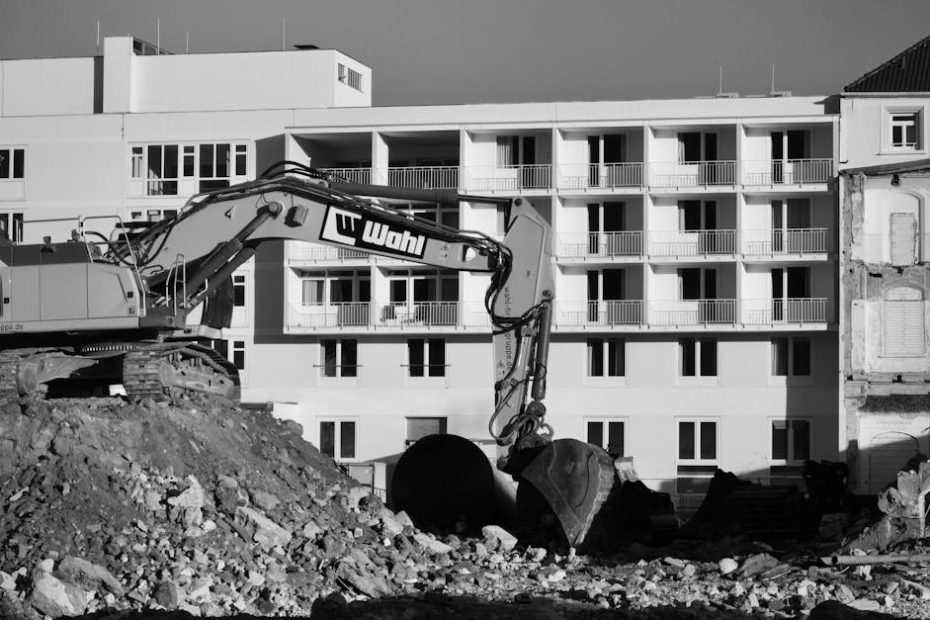Black and white image of an urban construction site with an excavator in front of a building.