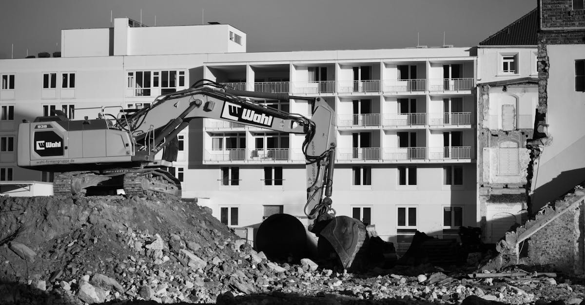 Black and white image of an urban construction site with an excavator in front of a building.